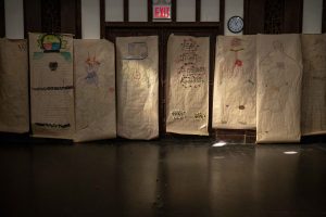 211106_MariaJoseWSGroup1_032 A row of colorful life-sized body maps hang in the back wall of a dimly lit church space.