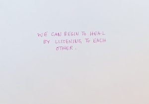 Pink text on a white background reading: We can begin to heal by listening to each other