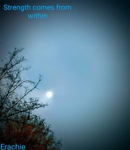 A small white moon in the middle of a blue sky at twilight. Some trees with green and red leaves in the lower left corner. At the top of the postcard, text reads: Strength comes from within. Text at the bottom of the postcard reads: Erachie